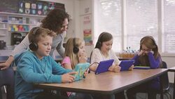 Elementary school aged children working on digital media tablets with teacher in classroom Stock Footage