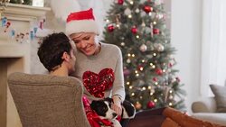 Affectionate couple cuddling with Jack Russell terrier in Christmas living room Stock Footage