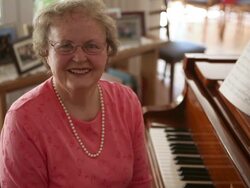 A static shot of a happy elderly woman sitting on a piano bench next to a piano. Stock Footage