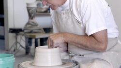 senior potter sitting at spinning pottery wheel shaping wet clay with his hands Stock Footage