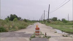 An orange barrel blocks traffic from a ruined, abandoned road following a flood in New Orleans. Stock Footage