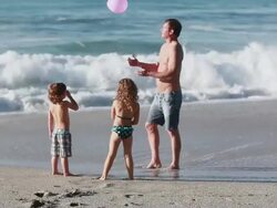 MS TS Boy and girl run to dad who has balloon then girl trips and falls and dad throws balloon and boy plays with it on beach / Montezuma, Puntarenas, Costa Rica Stock Footage