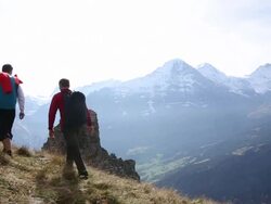 Wing suit fliers/ hikers ascend through mountain meadow Stock Footage