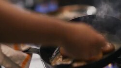 In restaurant kitchen, chef spoons oil and grease over sizzling scallops in iron skillet Stock Footage