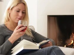 Female in front of fireplace drinking wine and reading book Stock Footage