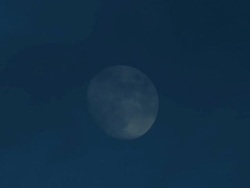 Time lapse of full moon passing through blue daylight sky with dark clouds Stock Footage