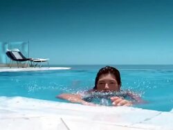 Medium shot woman swimming to edge of pool and smiling at CAM w/beach chairs in background Stock Footage