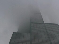 Low Angle tilt-up - Fog drifts over Willis Tower as it snows in Chicago, Illinois. / Chicago, Illinois, USA Stock Footage
