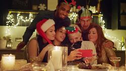 Playful friends in santa hats and reindeer antlers taking selfie at candlelight Christmas table Stock Footage