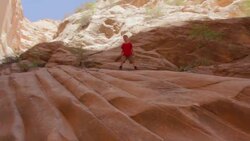 Young hiker boy stepping down a steep red-rocked canyon wall Stock Footage