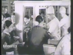 1942: JAPAN: FEMALE FACTORY WORKERS: WS Large crowd of female factory workers exiting lot. VS Females on line getting food, sitting together in groups at tables, eating w/ chopsticks. Home front Instructional Video