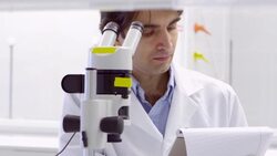 MS PAN Scientist taking notes while examining cell culture dish with microscope in research laboratory Stock Footage