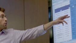 Trendy young businessman leads meeting in corporate boardroom, points out spreadsheet data on big-screen Stock Footage