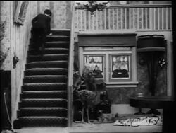 B/W 1916 Charlie Chaplin stumbling up stairs + rolling himself in rug while falling down stairs Stock Footage