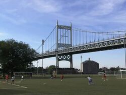 The Robert F. Kennedy Bridge - East River Span (formerly the Triborough Bridge) over a soccer field with boys practicing Stock Footage