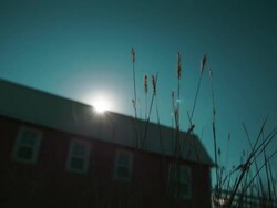 Timelapse of the sun rising from behind a barn with grass in the foreground Stock Footage