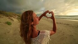 Female on beach makes heart shape finger frame to sunset Stock Footage