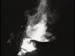 A pole stirs a fire in a pot, creating sparks. News Clip