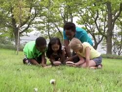 Diverse group of kids kneeling in grass with magnifying glass Stock Footage