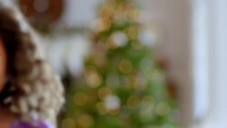 Cute young girl smiles at camera with Christmas tree in background (rack-focus) Stock Footage