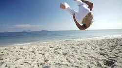 Brazilian capoeira fighter jumps and tucks his legs in an aerial flip on Ipanema Beach Stock Footage