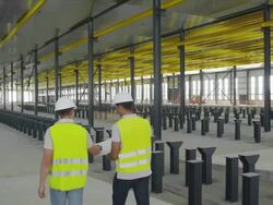 WS TS PAN two engineers in hi-viz vests walking down ramp and discussing plan in large, empty hangar; rear view, RED R3D 4K Stock Footage