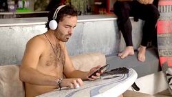 Young man with headphones waxing surfboard at surf shop Stock Footage