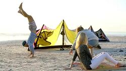 Young women watching man doing handstand on beach near kiteboarding equipment Stock Footage