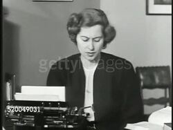 1946: WORKPLACE: DRAMATIZATION: Adult female, executive assistant, secretary, typing on typewriter at desk, looking up something in book. Adult male in suit approaching desk, female adjusting hair, taking business card from male, rising from desk. Instructional Video