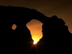 Two arches silhouetted in front of nice sunset with wispy clouds and deep colors Stock Footage