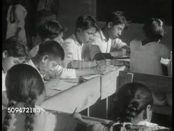1939: MEXICO CHILDREN: LS Concrete bridge. MS School building. INT VS Mexican elementary children at tables writing. MS Male teacher talking. MS Students raising hands. INT VS Doctor giving vaccination shot to little boy. Education, health, hospital Instructional Video