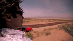 The passenger of a convertible car stands away from the highway looking out over the desert. Stock Footage