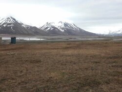 Two people riding their bicycles on an empty road through a picturesque arctic scenery with mountains covered by snow not far from Longyearbyen, the capital of the Norwegian Svalbard archipelago Stock Footage