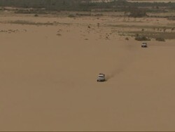 Medium Long Shot, tracking-left zoom-in - Two sport utility vehicles travel quickly across a long expanse of sand / Egypt Stock Footage
