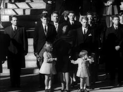 B/W 1963 Kennedy family standing outdoors at JFK's funeral / tilt down John Jr. salutes / newsreel Stock Footage