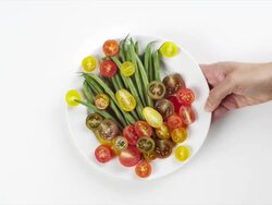 CU Woman hand entering setting down round white plate with green beans and delicate, multi-colored tomato slices / Omaha, Nebraska, United States Stock Footage