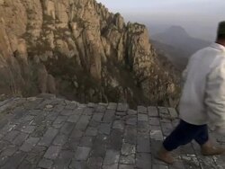 A Chinese man walking along the Great Wall of China, with a beautiful example of China's unique mountains in the background.  Stock Footage