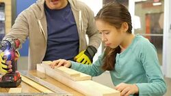 Hispanic man teaches elementary age Hispanic girl how to use drill in a children's camp at a community workshop Stock Footage