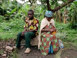 MS Shot of ugandan man and woman sitting on log, man looking towards and woman  weaving  basket / kigez, kabale, uganda Stock Footage