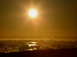 WS T/L View of Sun moving across orange sky as it sets over ocean filled with icebergs / Ilulissat, Greenland Stock Footage