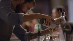 Skilled bartender pours mixed drink into glass from cocktail shaker Stock Footage