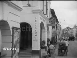 1953: KUALA LUMPUR, MALAYA: HA (POV Moving vehicle) WS Side street w/ pedicabs, people walking, driving toward local meeting place Coliseum Cafe & Hotel (shaky). WS Rubber plantation estate manager Tony Hooper out of armored car, walking into building. Instructional Video