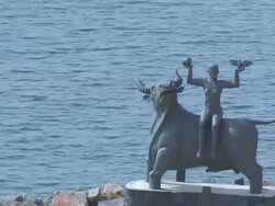 MS AERIAL Shot of Zeus statue with Europa and bay at distance / Agios Nikolaos, Crete, Greece Stock Footage