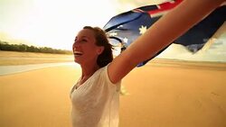 Young woman on the beach at sunset holding an Australian flag in the air Stock Footage