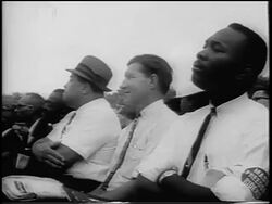 B/W August 28, 1963 low angle 3 Black + White men sit watching speech / March on Washington / newsreel Stock Footage