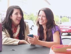 MS Two young girls using cellular device at table outside in outdoor mall smiling and having fun / Minneapolis, Minnesota, United States Stock Footage