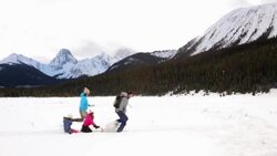 Family running sledding in snowy field below mountains Stock Footage