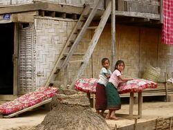 MS SLO MO Shot of Two children leaning on red mattress placing on table sometimes looking at towards near primitive looking structure with other red mattress and sheet hanging / Village near Luang Prabang, Laos Stock Footage