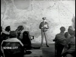 1942 REPRISAL: MISSION BRIEFING: Officer explaining SOT mission to different crew in another location, target is assembly plant at Marienberg (Germany) PAN US Combat Crew listening to briefing, one male holding small terrier dog, mascot. WWII Instructional Video