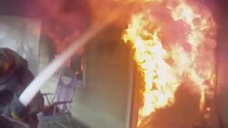 Slow Motion firefighter POV, standing at doorway of burning home, spraying water into fire Stock Footage